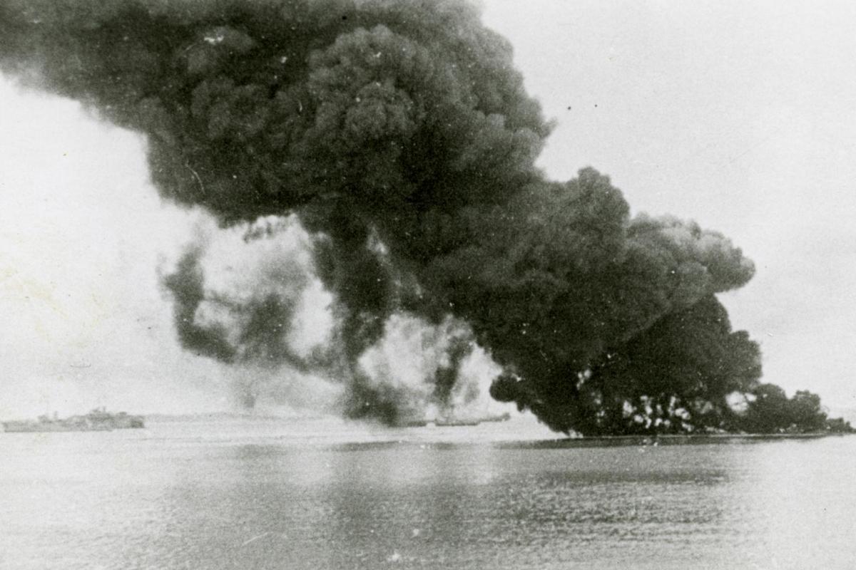 The impact of the first air raid on shipping with (L-R) the HMAS Swan; Floating Dock AFD18; SS Zealandia burning and sinking; HMAS Wato (tug); HMAS Platypus (obscured); oil burning from sunken USS Peary.