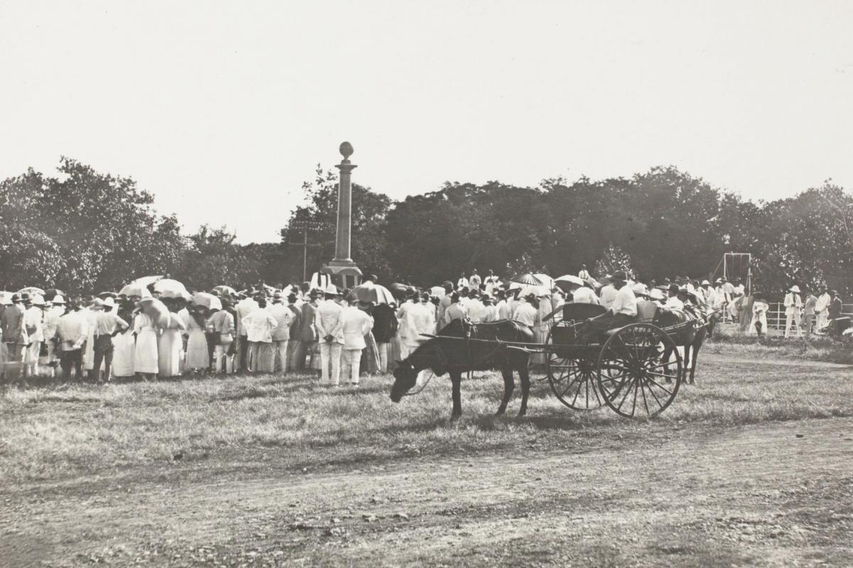 A large crowd of men and women surround the Cenotaph at centre. A horse and buggy stand in the foreground.
