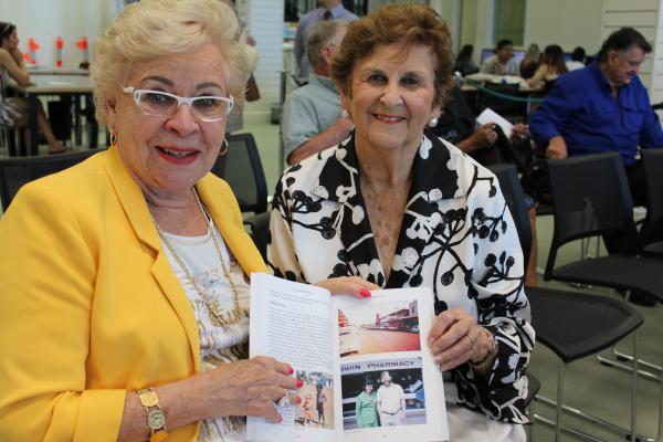 Two senior women, woman on left wearing bright yellow jacket and woman on right in black and white patterned blouse holding one of the 2018 book entires