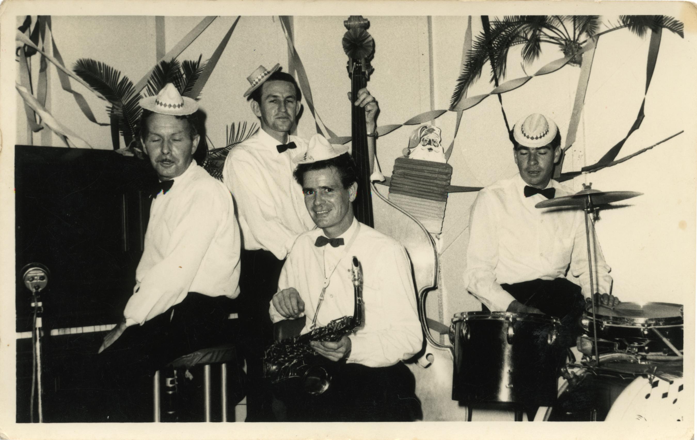 Black and white photo of four men dressing in white shirt and bow ties playing musical instruments. in