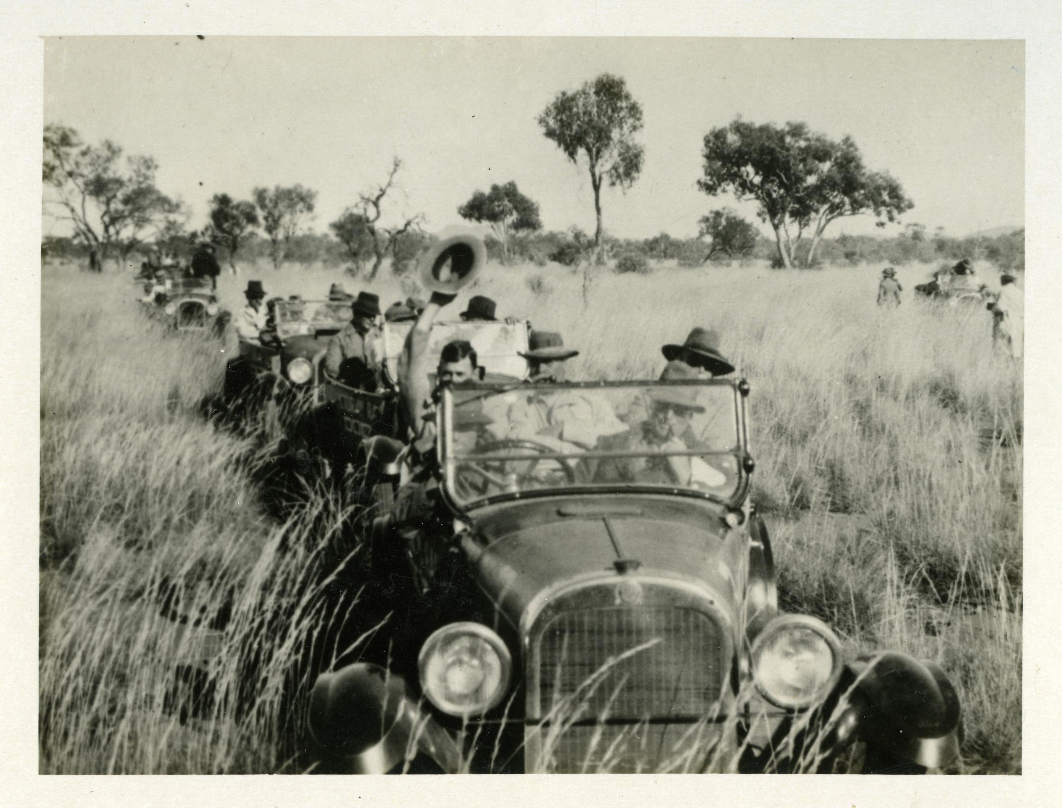 Convoy of old fashioned cars with men driving through the outback of the Northern Territory. Black and white image.