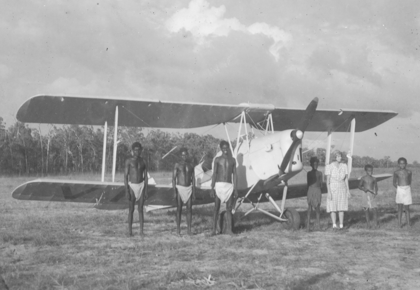 European woman posing alongside six Aboriginal boys in front of a tiger moth aeroplane