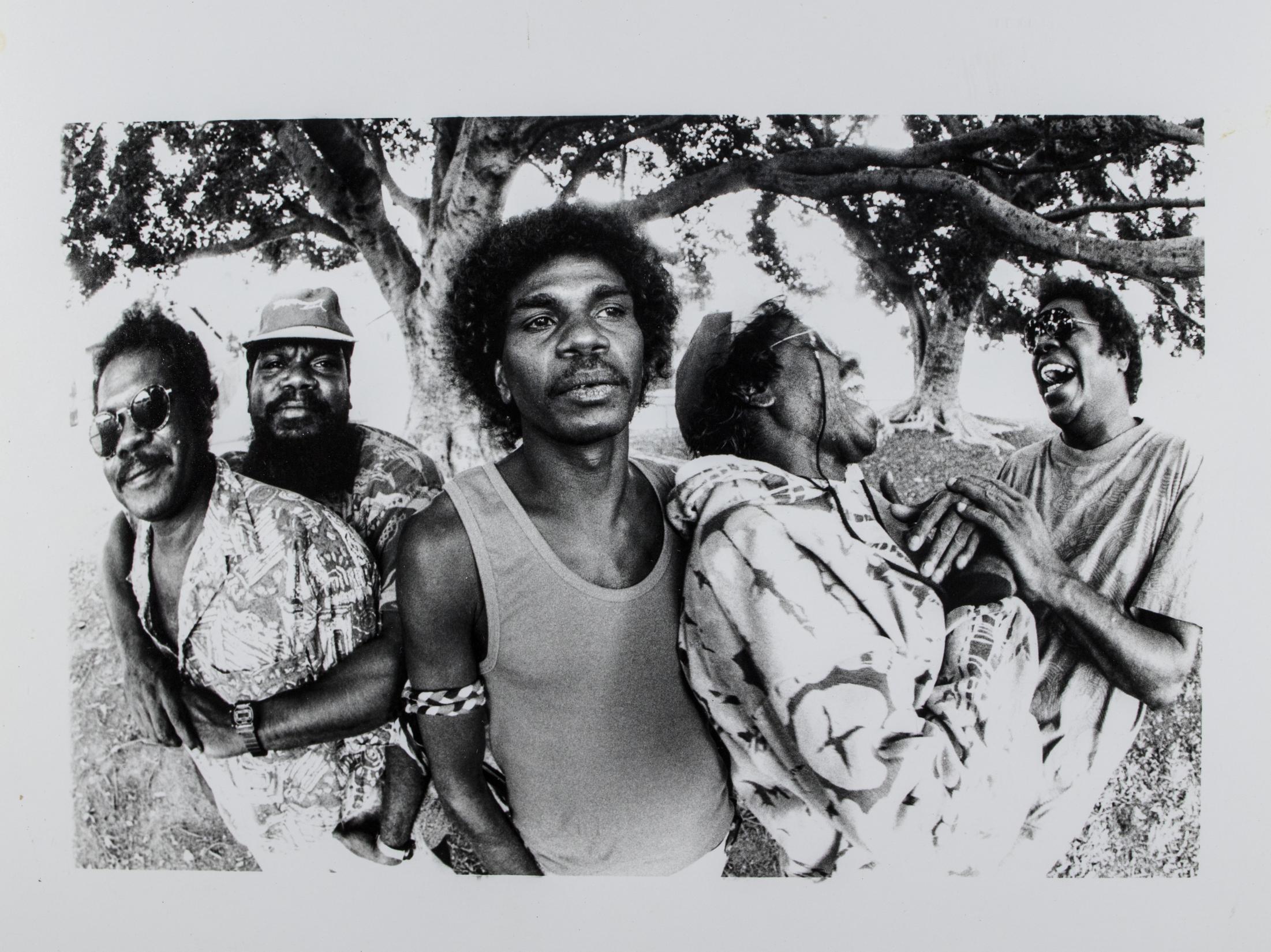 Black and white photograph of five men from Sunrize band posing for photo. Come men laughing others staring into the distance