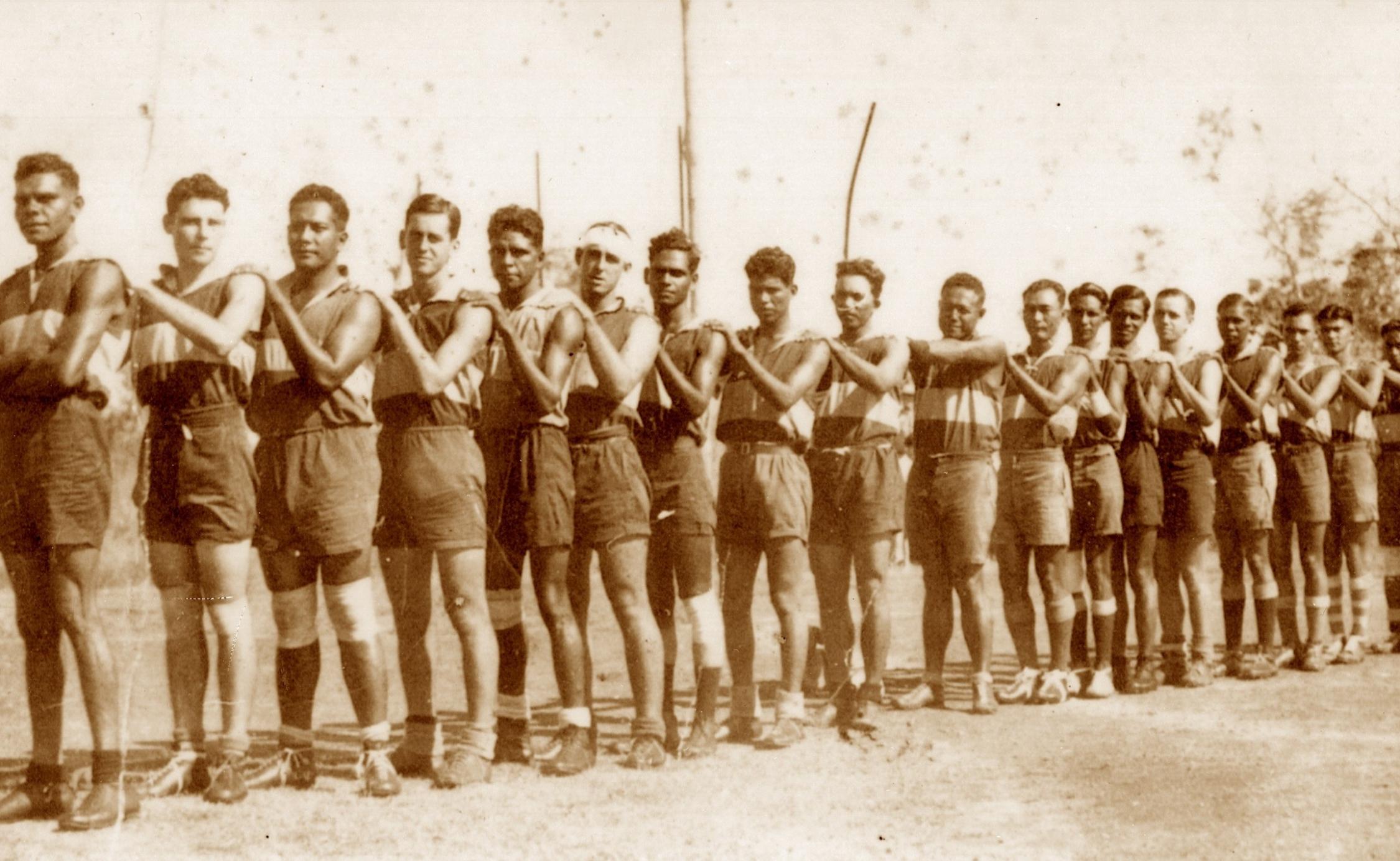 Sepia coloured photograph of the Buffalo football team lined up at an angle with their hands resting on the shoulders of the person in front of them