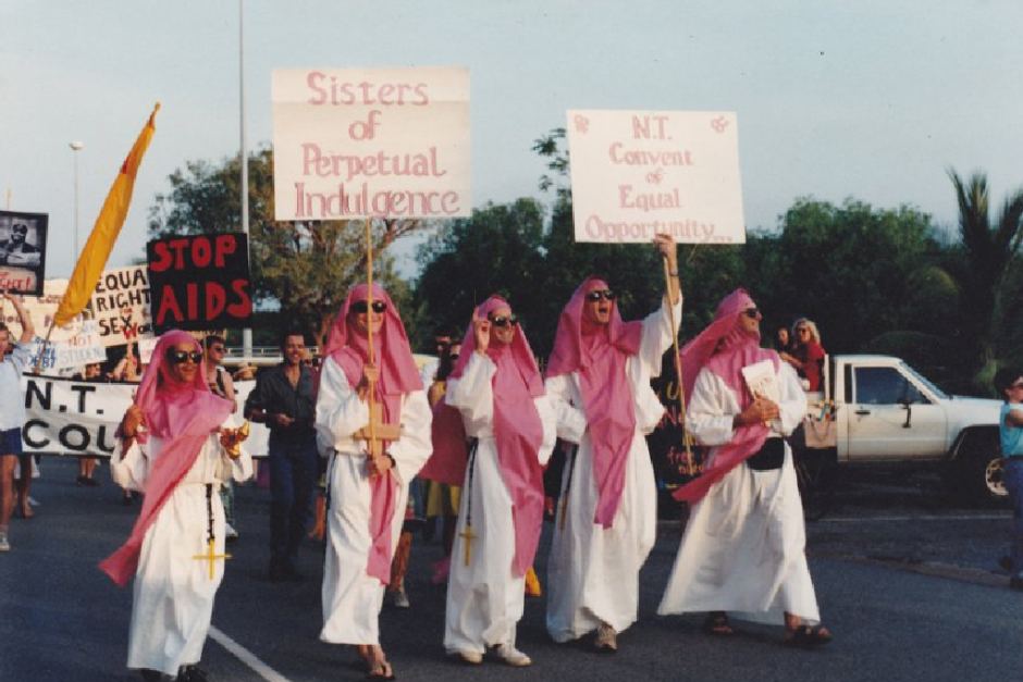 Five men dressed in white robes and red head scarves marching with placards that reads "Sisters of Perpetual Indulgence". March is part of the Gay Pride March in Darwin. 