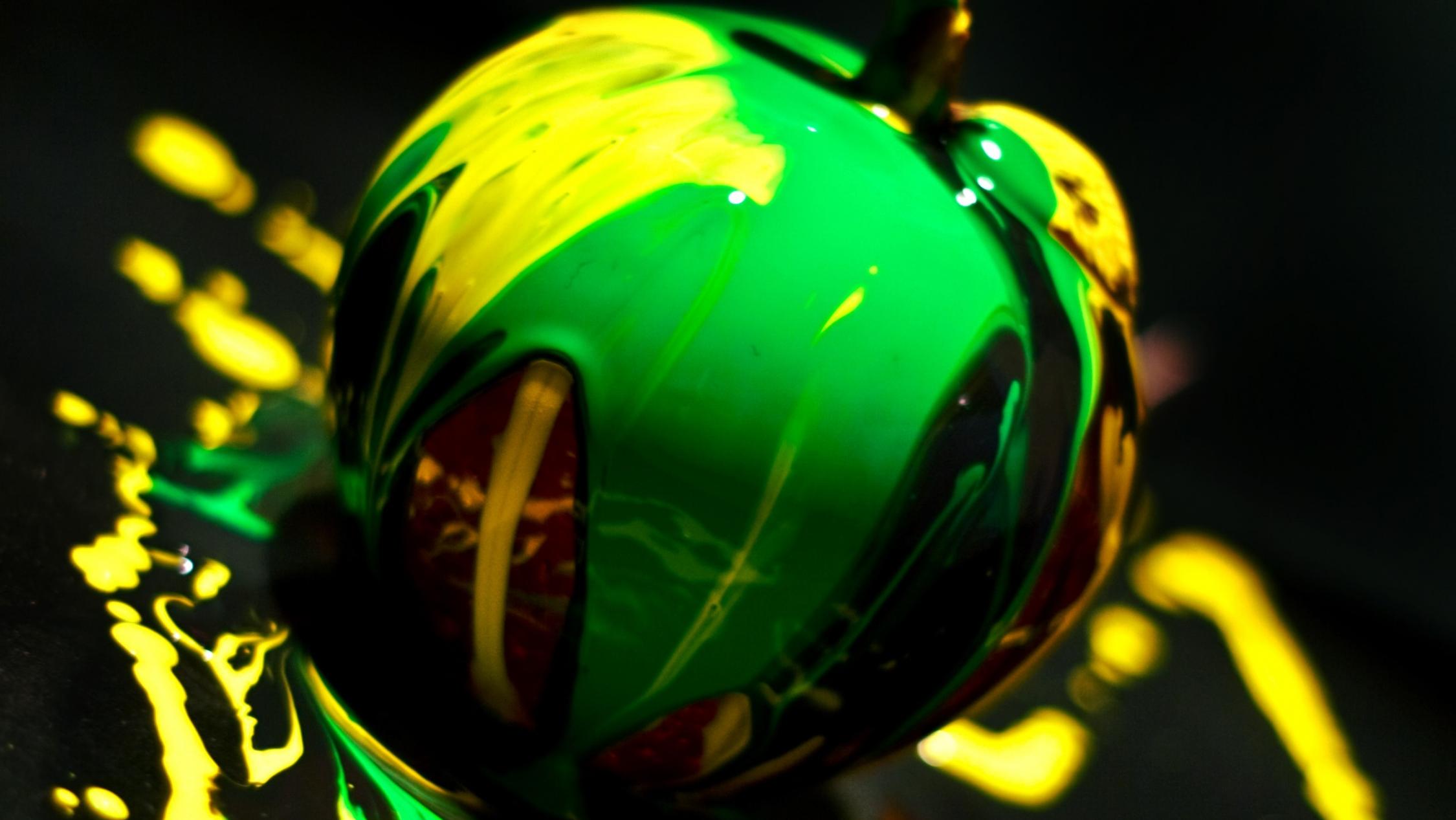 apple covered in green and yellow paint set against a black backdrop