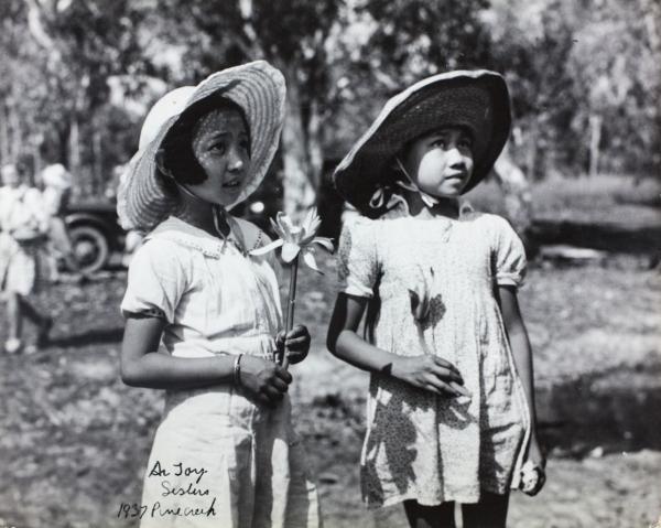 Black and white photo. two girls wearing sunhats and holding water lilies 